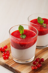 Vegan dairy free coconut Panna cotta with strawberry sauce in glasses on white wooden table. Healthy dessert. Vertical orientation.