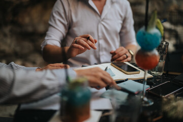 Casual business meeting outdoors showcasing teamwork and collaboration with digital devices, notebooks, and refreshing drinks. Professionals discussing ideas in a relaxed, open-air setting.