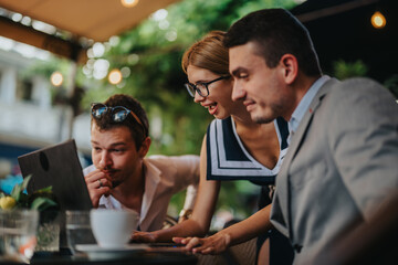 Businesspeople collaborating on a laptop at an outdoor cafe. They exhibit teamwork and communication in a relaxed and productive setting.