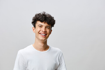 Smiling young man with curly hair on a neutral background, showcasing happiness and confidence Friendly demeanor highlights positive energy and approachability