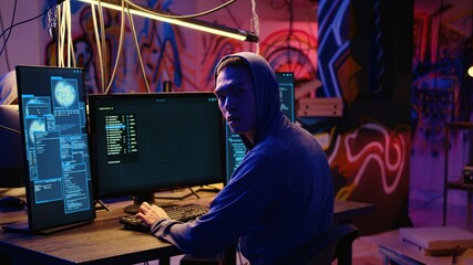 Asian hacker hiding in underground bunker, looking over his shoulder and feeling anxious after stealing data from victims using computer virus, scared about being caught by police