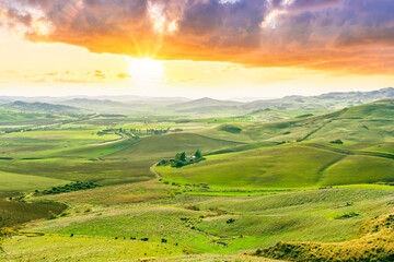 beautiful rural view at summer or spring season fields and hills with rustic grassland and nice mountains with blue cloudy sky on background of countyside landscape