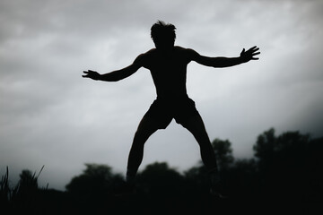 Silhouette of a man in mid-air practicing high jumps against a cloudy, dramatic sky and natural outdoor setting