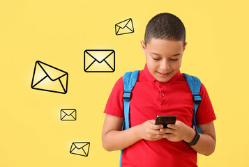 Happy little African-American schoolboy with backpack and mobile phone on yellow background