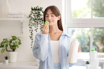 Young woman smelling laundry detergent at home