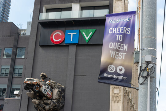 projecting hanging banner at Queen Street West (Cheers to Queen West) with defocused Bell Media building (CTV) behind at about 299 Queen St W in Toronto, Canada