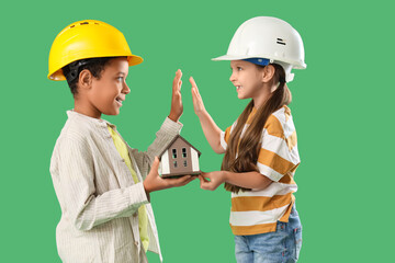 Cute little architects with house model giving high-five to each other on green background