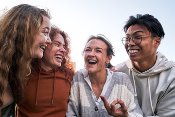 Portrait of a group of four students having fun outdoors and they are hugging. The photo is taken...