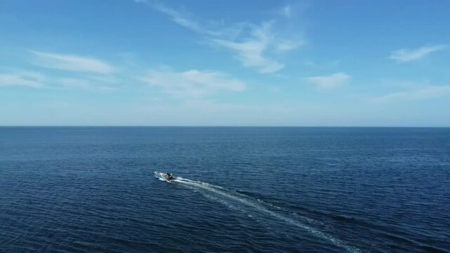 Un p&ecirc;cheur en chaloupe a moteur navigue rapidement sur une mer calme se fondant avec l'horizon r&eacute;fletant le bleu du ciel et les reflets du soleil rayonnent sur les vagues. ( Fleuve Saint-Laurent )
