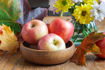 Apples in bowl, flowers and fall leaves, autumn season or Thanksgiving holiday concept, horizontal