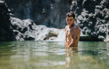 Fototapeta premium Young man taking a swim in a serene natural pool with rocky surroundings, enjoying a peaceful and refreshing moment in nature.