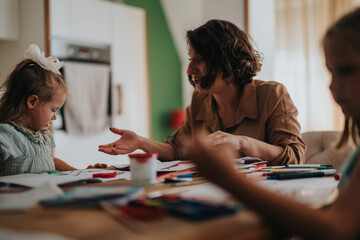 Fototapeta premium A mother and her daughters engage in a creative drawing session at their cozy home, fostering creativity and bonding. The warm, inviting environment highlights familial love and togetherness.