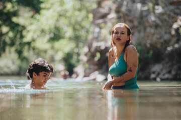 Two young people swim in a serene natural pool surrounded by lush greenery, enjoying a beautiful and refreshing summer day.