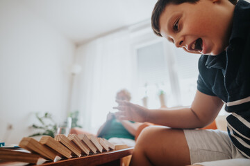 A young boy enthusiastically plays with building blocks while his grandmother knits a vest in the...
