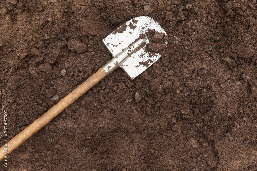 Wall mural brown dark soil ground texture background with copyspace and shovel top view