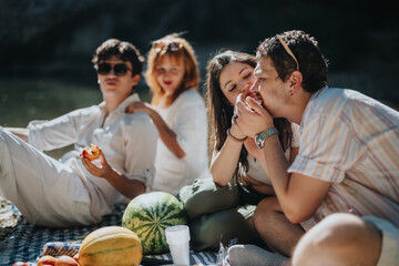 A group of young friends relaxes by the water, savoring fresh fruit and enjoying each other's company on a sunny day picnic.