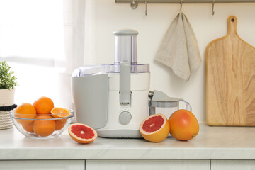 Modern juicer and grapefruits on white counter in kitchen