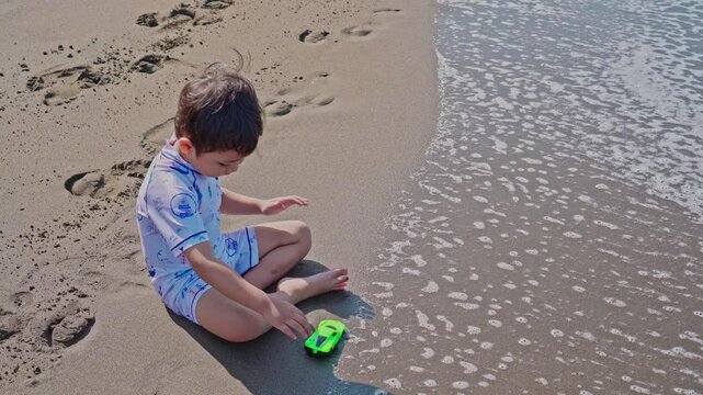 Little boy sitting on the beach, playing with cars and sand in the morning. Child playing alone in summer vacation