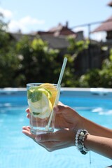 Woman holding tasty cocktail in glass near swimming pool outdoors, closeup