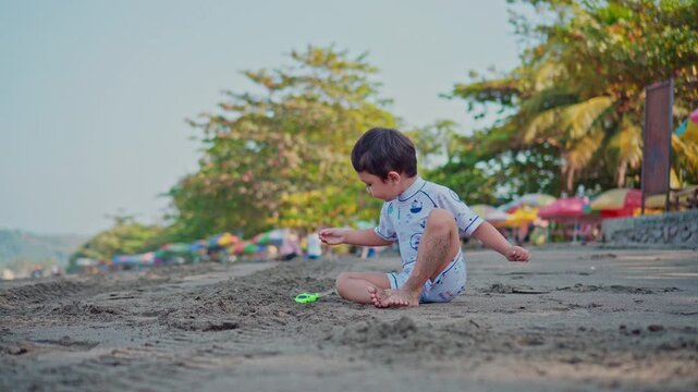 Little boy sitting on the beach, playing with cars and sand in the morning. Child playing alone in summer vacation