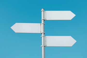 A white street sign with an arrow pointing to the left. The sign is on a pole and is in the sky