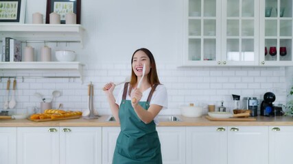 Young Asian woman dancing in the kitchen. The joy of a beautiful woman relaxing in her free time during the weekend in the house