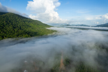 Aerial view drone shot of flowing fog waves on mountain tropical rainforest,Bird eye view image over the clouds Amazing nature background with clouds and mountain peaks