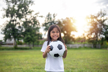 A young girl is holding a soccer ball in a park