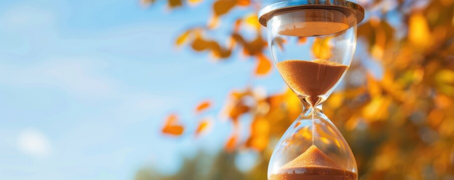 Close-up of an hourglass with flowing sand, set against a backdrop of autumn leaves, symbolizing the passage of time.