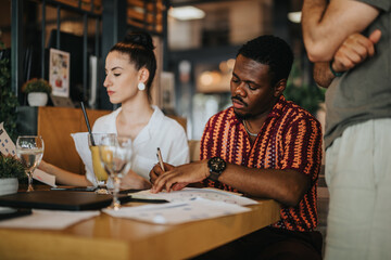 Diverse group of colleagues collaborating in a casual business meeting at a coffee bar, discussing ideas and taking notes.