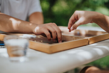 Close-up of two hands engaged in a friendly board game outdoors, capturing a moment of leisure and strategy.