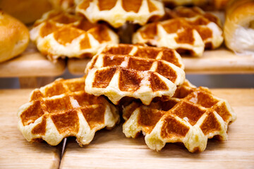 Golden brown Belgian waffles stacked on a wooden board, showcasing their crispy exterior and soft, fluffy texture. Perfect for breakfast or a sweet snack.
