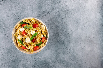 Italian cold salad with fusilli pasta, cherry tomatoes, mozzarella, arugula. Top view. Copy space.