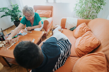 A grandmother and teenager engage in a board game on the living room table, fostering family bonding and leisure time. The cozy setting is filled with warm tones and indoor plants.