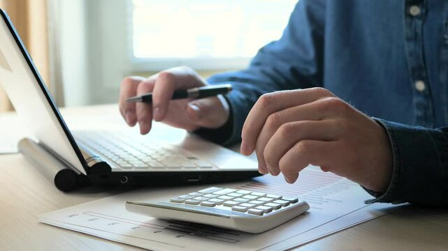 Hands of a businessman close-up, in the office on a table with items for doing business. A businessman using a calculator and a computer calculates the data of a global financial report. Slow motion.