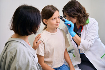 Fototapeta premium Medical worker uses special instrument to examine teenage girls ear