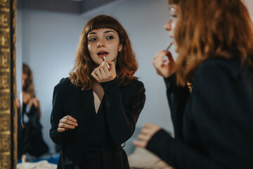 A young woman carefully applies lipstick in front of a mirror, preparing herself for a night out. The mood is focused and anticipatory, capturing the essence of getting ready.