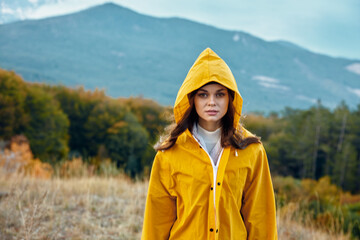 Woman in a yellow raincoat enjoying the scenic view of mountains in a tranquil field on a rainy day