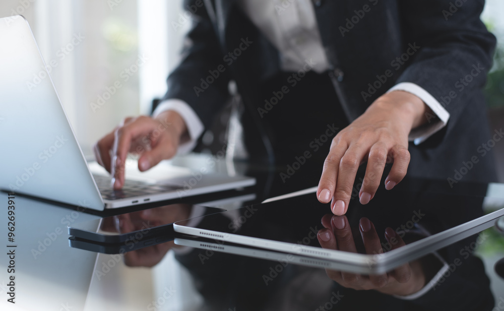 Wall mural Businesswoman working on laptop and using digital tablet on office table, closeup