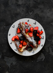 Croissant French toast with powdered sugar, strawberries and blackberries on a dark background, top view