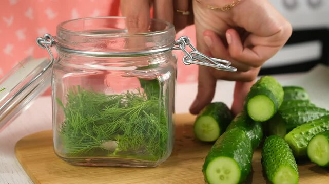 Woman putting cucumbers with dill, garlic in glass jar to cook pickles on kitchen, hands close-up. Cuisine, culinary, prepare cook dish, domestic food, recipe, fresh organic ingredients concept.