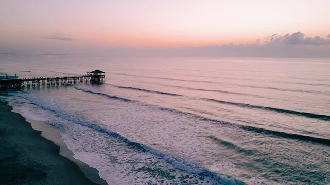 A peaceful sunrise over the ocean with gentle waves near a pier