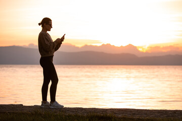 Silhouette of a Woman Using Technology at Sunset by the Lake Ohrid