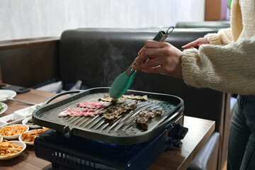 A woman hands putting meat into the skillet on the stove in the