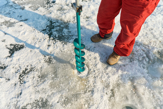 A warmly dressed Asian guy drills a hole in the ice on winter fi