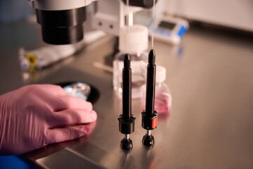 Gloved hand adjusting equipment under a microscope in a lab