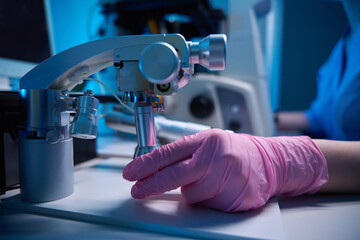 Gloved hand adjusting a micromanipulator under a microscope in laboratory