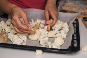 A person s hands preparing a baking tray with cauliflower florets and breaded chicken pieces, ready for the oven. Emphasizes the blend of fresh vegetables and protein for a balanced diet.