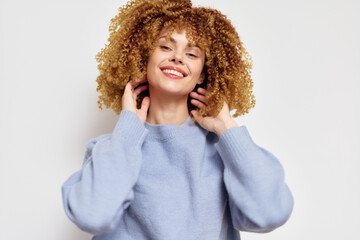 Smiling woman with curly hair in a light blue sweater against a plain white background, exuding happiness and confidence, perfect for beauty and fashion themes