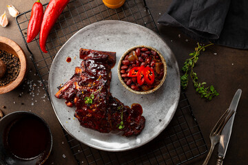 Roasted Pork Ribs in BBQ Sauce with Red Beans in the plate and dark background top view